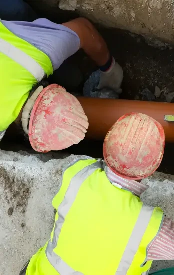 Two plumbers in hard hats repairing a pipe in a trench